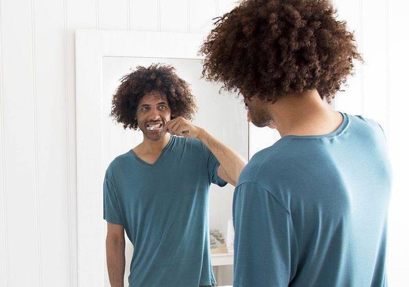young man brushing teeth in front of mirror