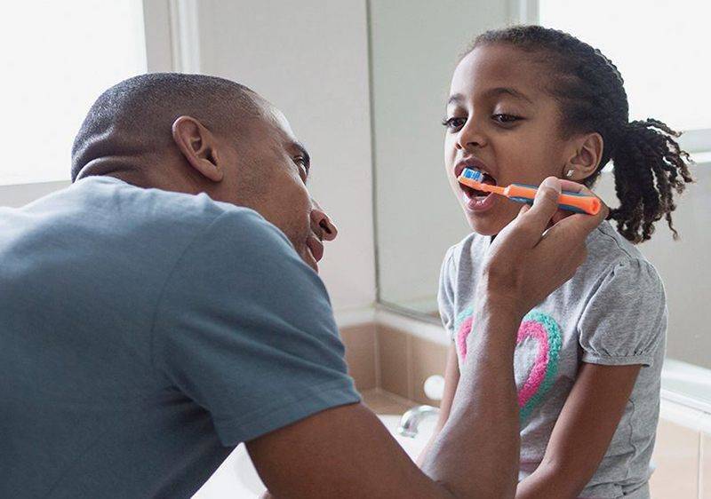 dad teaching young daughter to brush her teeth