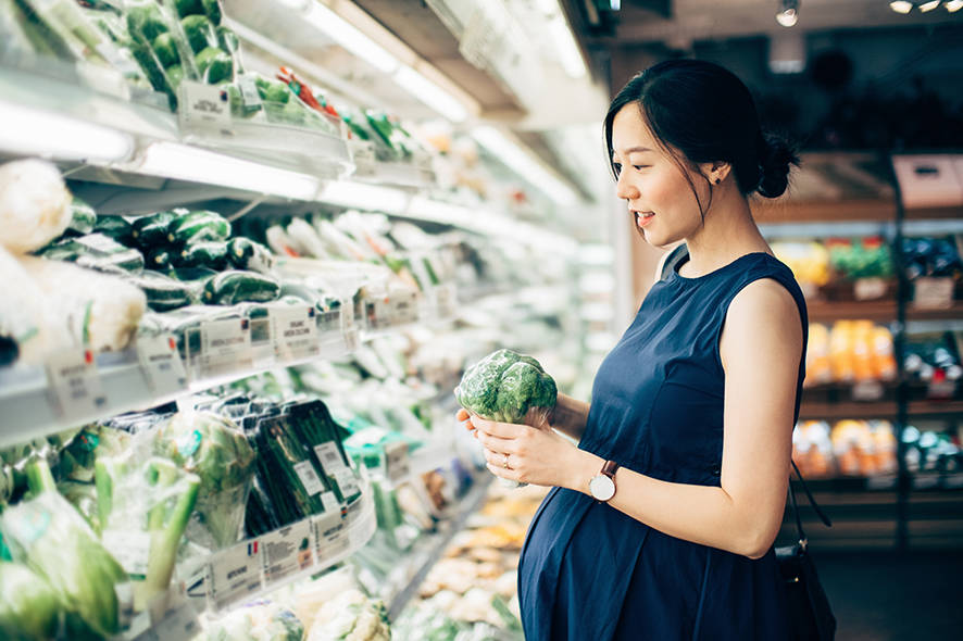 Pregnant lady in the supermarket looking at vegetables